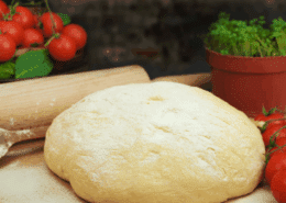 Bola de masa de pizza junto con harina, tomate y albahaca